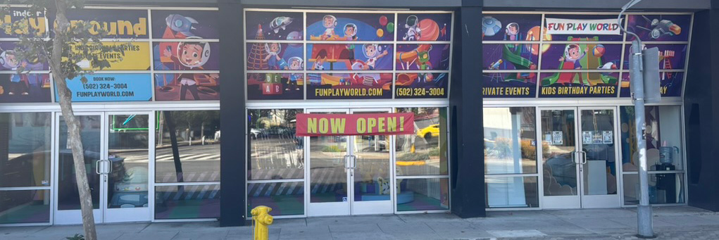 Storefront of a children's play center called Fun Play World with colorful cartoon banners in the windows and a large 'NOW OPEN!' sign above the entrance.