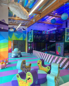 Colorful indoor children's play area with animal-shaped seats, foam flooring, and a ball pit.