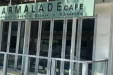 Exterior view of Marmalade Cafe storefront with a green sign that reads 'MARMALADE CAFE' and 'Breakfast · Lunch · Dinner · Catering'. The glass doors and metal railing are visible.