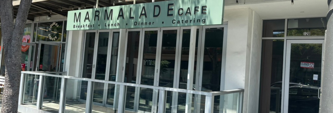 Exterior view of Marmalade Cafe storefront with a green sign that reads 'MARMALADE CAFE' and 'Breakfast · Lunch · Dinner · Catering'. The glass doors and metal railing are visible.