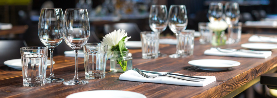 Table set for dinner with wine glasses, water glasses, plates, and a small white flower centerpiece.