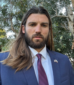 a man with long brownhair, a beard and mustache is wearing a white shirt and blue sport coat with a tie