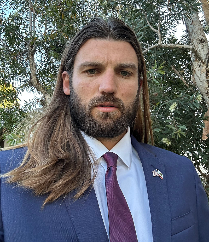 a man with long brownhair, a beard and mustache is wearing a white shirt and blue sport coat with a tie