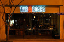 Night view of Tar & Roses restaurant on Santa Monica Blvd, with diners inside through large glass windows.